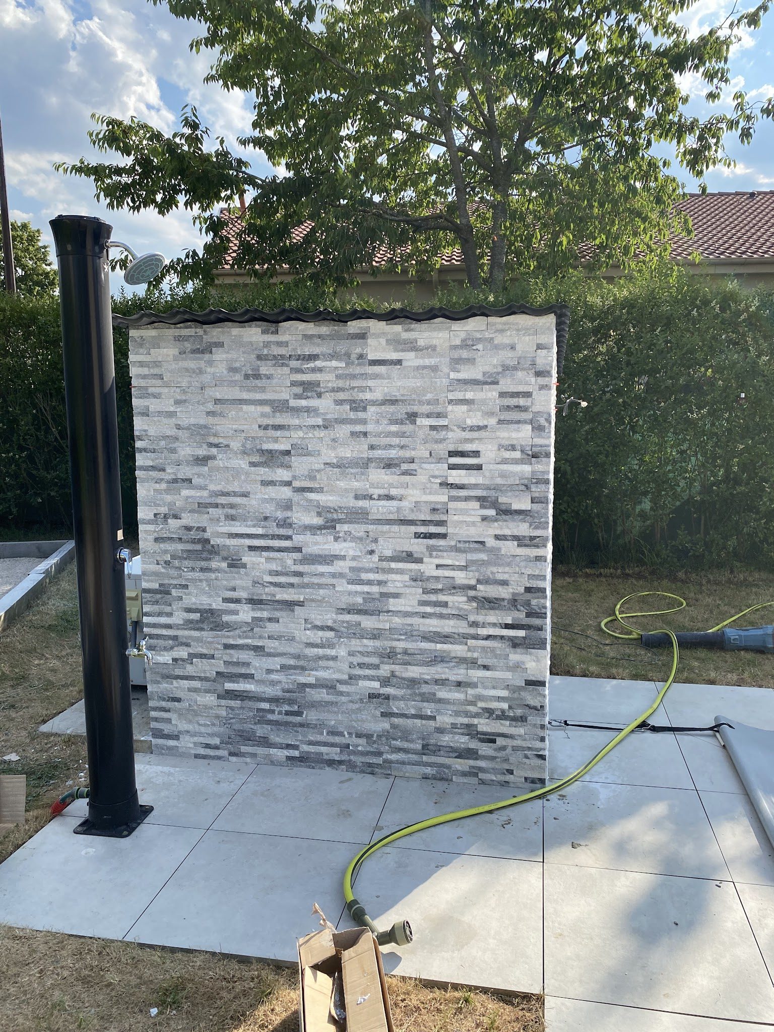 Douche extérieure : dalles sur le gazon et mur en plaquettes de pierre